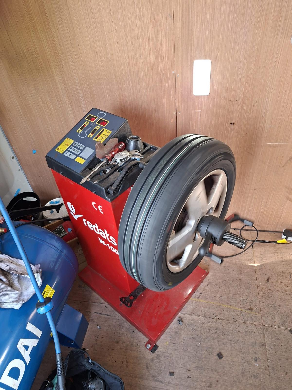 Red wheel balancing machine spinning a wheel inside the EJW van, with tools and air compressor